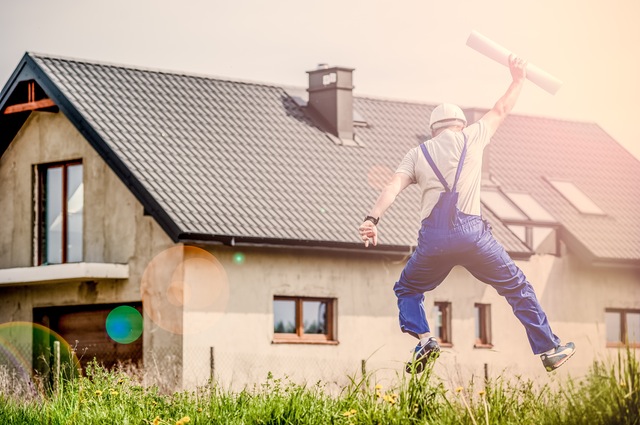 Foto de um engenheiro pulando de felicidade com a planta de um imóvel em mãos em frente a uma casa para a pauta "Condomínio Novo: Dicas Importantes Para uma Mudança Tranquila" do Blog da Estasa.