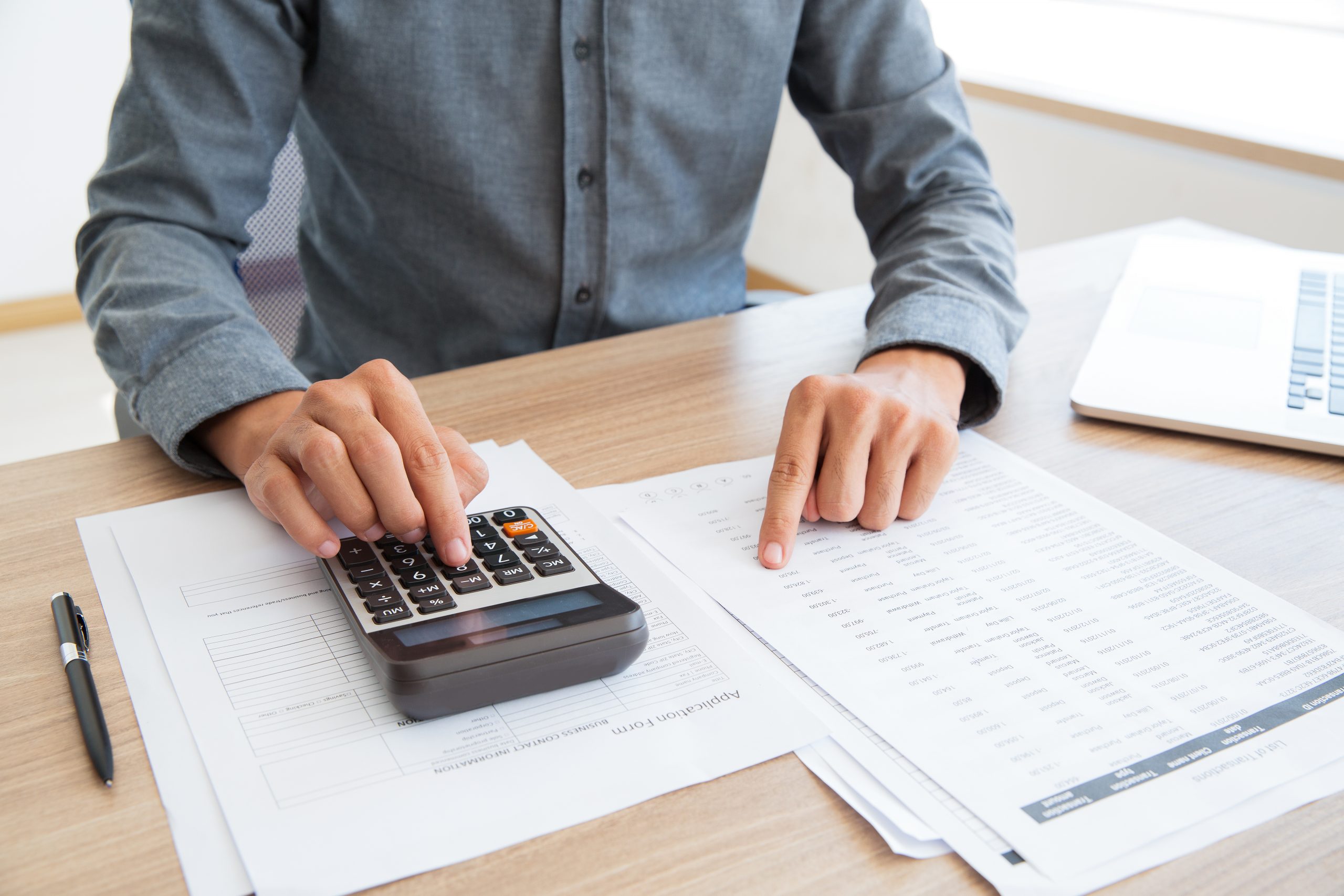 Foto de uma pessoa mexendo em uma calculadora em cima de uma pilha de papéis para a pauta: "Contas a pagar, uma das etapas mais complexas da administração condominial" para o Blog da Estasa